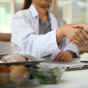 Cropped shot of dietitian in white coat shaking hands with patient at clinic.