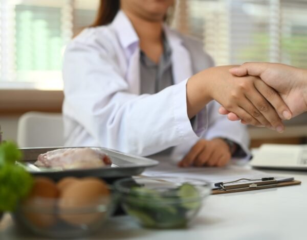 Cropped shot of dietitian in white coat shaking hands with patient at clinic.